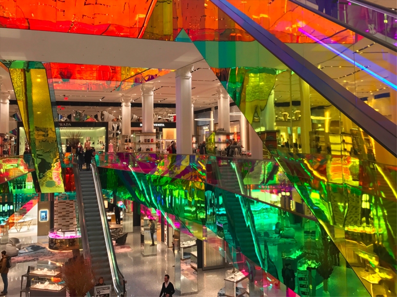 Designed by Rem Koolhaas, the new dichroic film-coated escalators at Saks not only twinkle, but also throw flashes of color on the white walls and columns. (Photo by Theadora Brack)